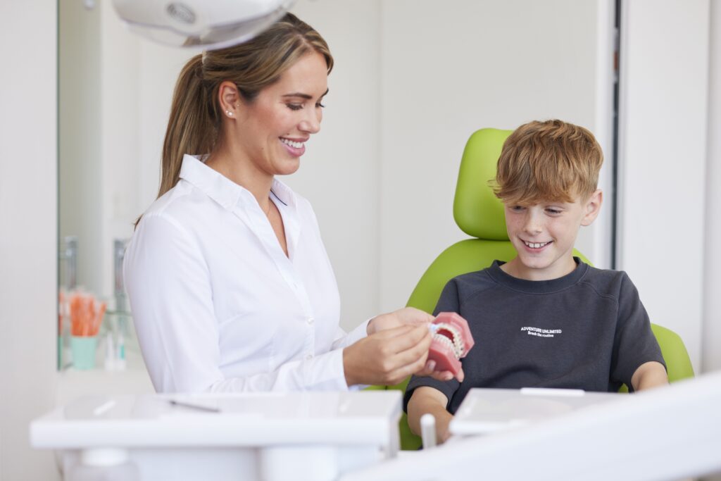 Kieferorthopädin Dr. med. dent. Jennifer Hoppe erklärt einem jungen Patienten anhand eines Zahnmodells die Vorteile einer losen Zahnspange. Beide befinden sich in einem Behandlungsraum der kieferorthopädischen Fachzahnarztpraxis Biss & Bogen in Ratingen-Lintorf.