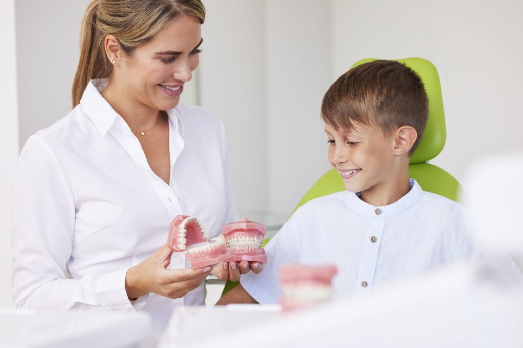 Kieferorthopädin Dr. med. dent. Jennifer Hoppe aus der Praxis Biss & Bogen erklärt einem jungen Patienten mithilfe eines Zahnmodells die Behandlung.