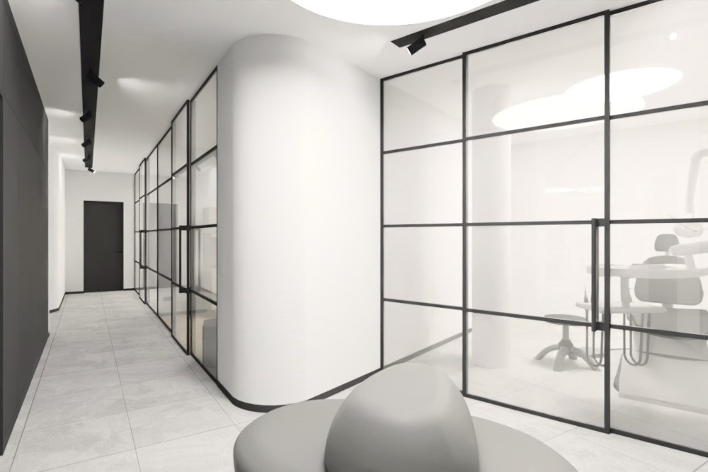 Heller, moderner Flur einer neuen kieferorthopädischen Praxis in Düsseldorf. Links führt ein langer Gang mit hellgrauen Bodenfliesen und einer dunklen Wand entlang; an der Decke sind schwarze Schienenstrahler angebracht. Rechts grenzen bodentiefe Glaswände mit schwarzen Metallrahmen mehrere Räume ab. Durch eine Glastür ist ein Behandlungszimmer zu sehen, mit einem KFO-Behandlungsstuhl, Instrumenteneinheit und einem kleinen Hocker. In der Mitte steht eine abgerundete, weiße Wand bzw. Säule, die den Flur weich gliedert. Im Vordergrund ist unscharf eine graue Sitzgelegenheit erkennbar. Insgesamt wirkt alles minimalistisch, sehr sauber und modern.